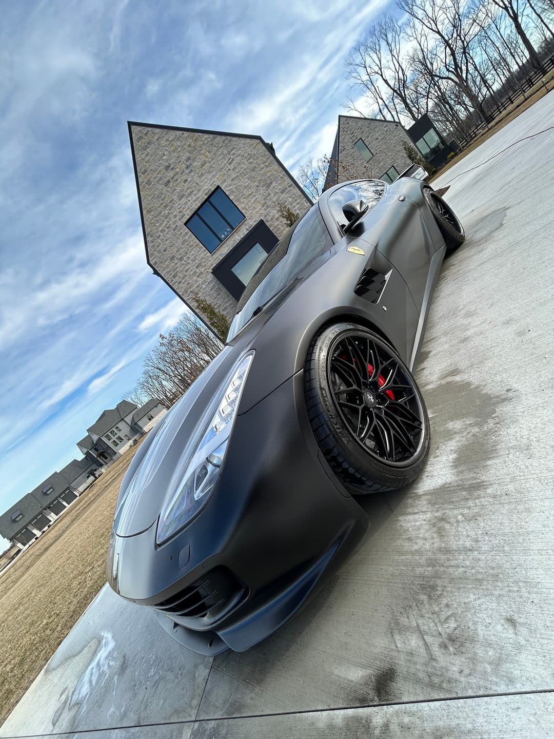 Luxury matte black sports car with sleek design parked outside modern stone houses.