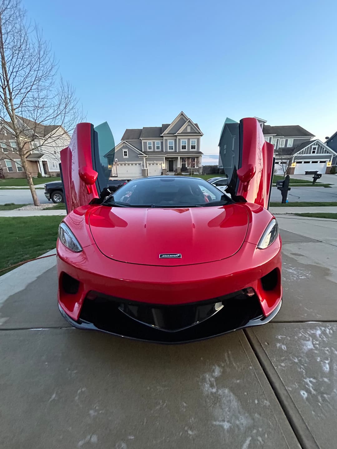Red sports car with butterfly doors open, parked in residential driveway at sunset.